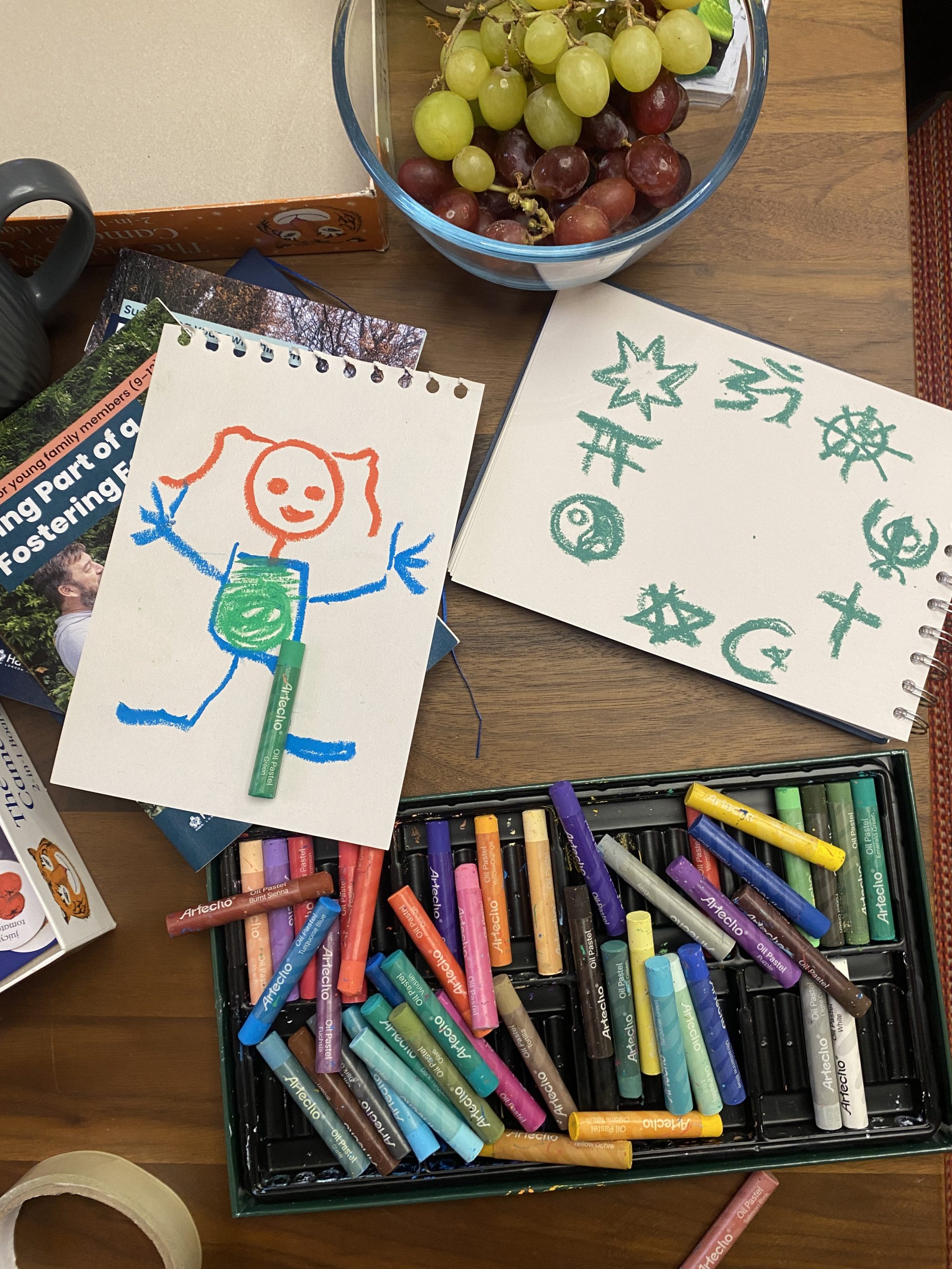a table with colours and drawings, including a drawing of a stylised little girl and one showing different faith symbols